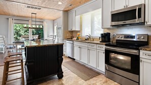 Una cocina moderna con armarios blancos, una isla central, electrodomésticos de acero inoxidable y techo de madera.