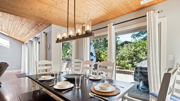 Comedor con una mesa de madera oscura dispuesta para cuatro personas, sillas blancas y una lámpara colgante.
