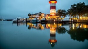 Un puerto deportivo con barcos amarrados, un faro y un edificio con iluminación cálida.