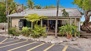 A small, single-story building with a metal roof, surrounded by tropical plants and a parking area. - **SET SAIL @ COCONUT MALLORY** Condo + Last Key White Glove Service... (Key West)