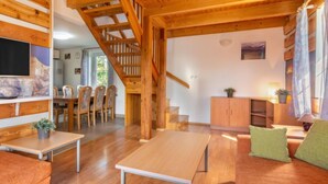 Ein gemütliches Wohnzimmer mit einer Holztreppe, einem Essbereich und einer im Hintergrund sichtbaren Küche.