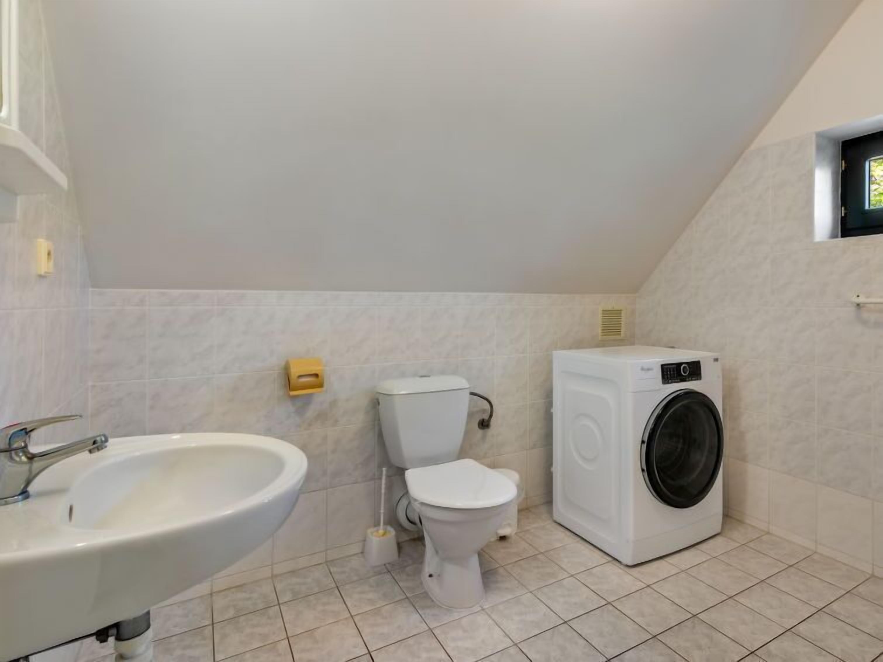 A small, modern bathroom with a sink, toilet, and washing machine.
