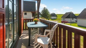 Ein Balkon mit Tisch und Stühlen, mit Blick auf eine ländliche Landschaft mit Häusern und einem Auto.