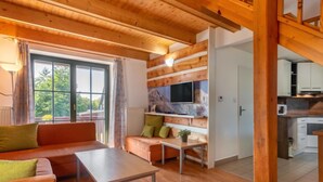 Ein gemütliches Zimmer mit Holzboden, einer Couch, einem Tisch und einem an einer Holzwand montierten Fernseher.