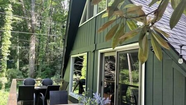 Ett tvåvåningshus med en veranda, utomhusmöbler och stora fönster.