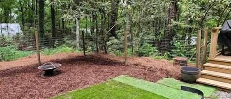 A garden area with a wooden deck, a fire pit, and a fenced area with trees.