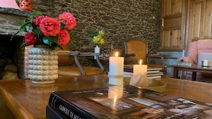 A book titled 'UN VIVE EN EL TEMPO' on a wooden table, surrounded by candles, a vase with flowers, and a stone wall in the background.