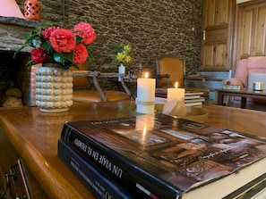 A book titled 'UN VIVE EN EL TEMPO' on a wooden table, surrounded by candles, a vase with flowers, and a stone wall in the background.