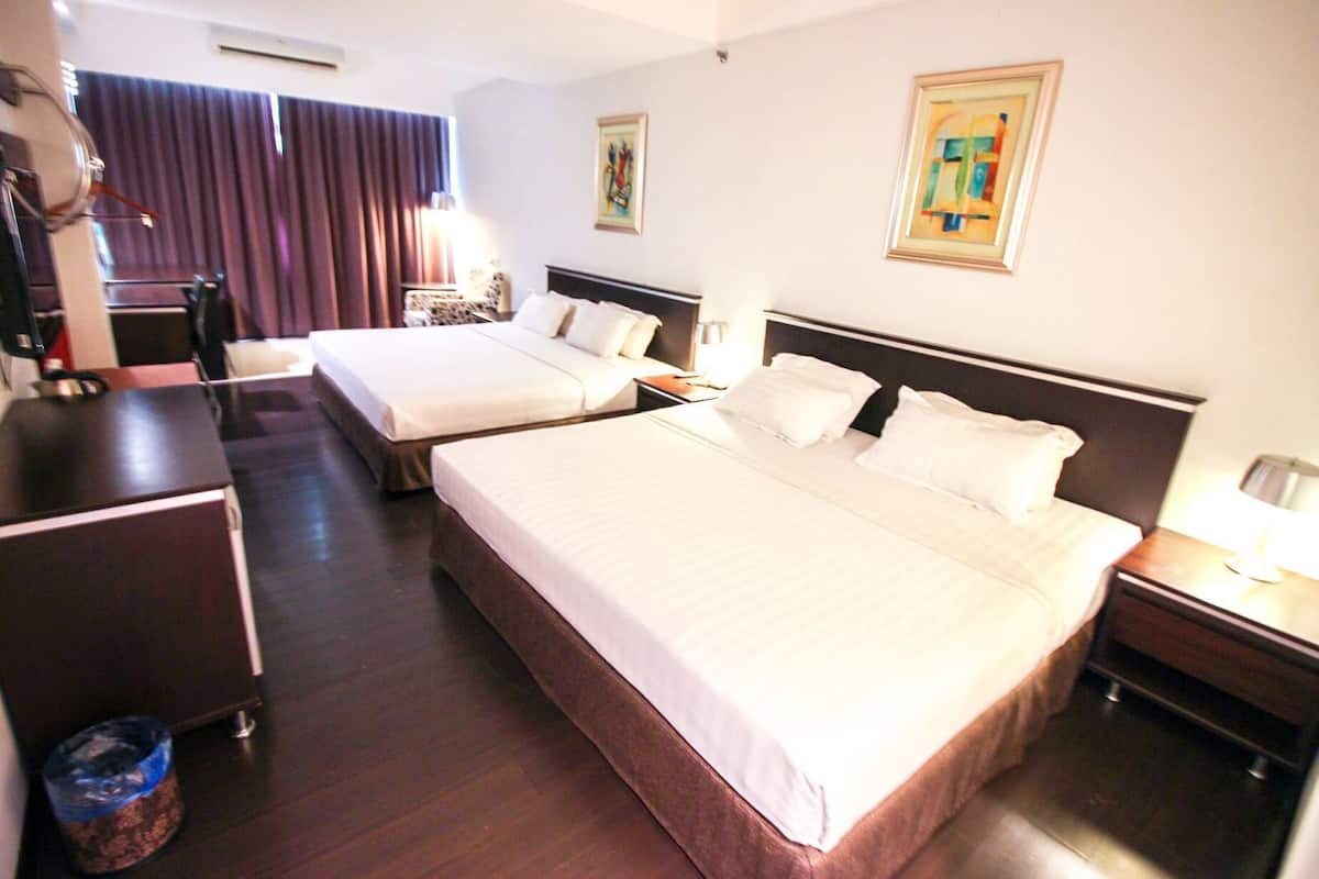 Habitación de hotel con dos camas, un escritorio, una silla, un cubo de basura y obras de arte en las paredes.