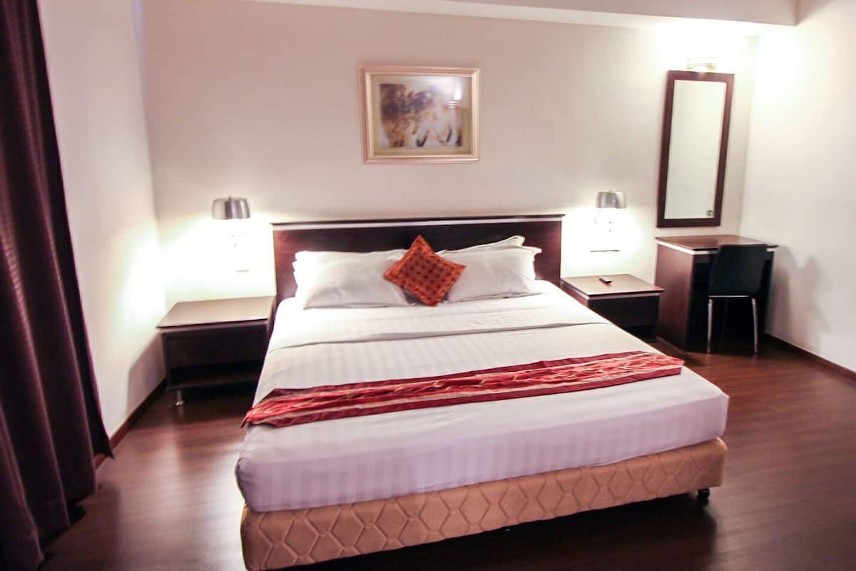 Una habitación de hotel con una cama, dos mesitas de noche, un escritorio, una silla, un espejo y un cuadro en la pared.