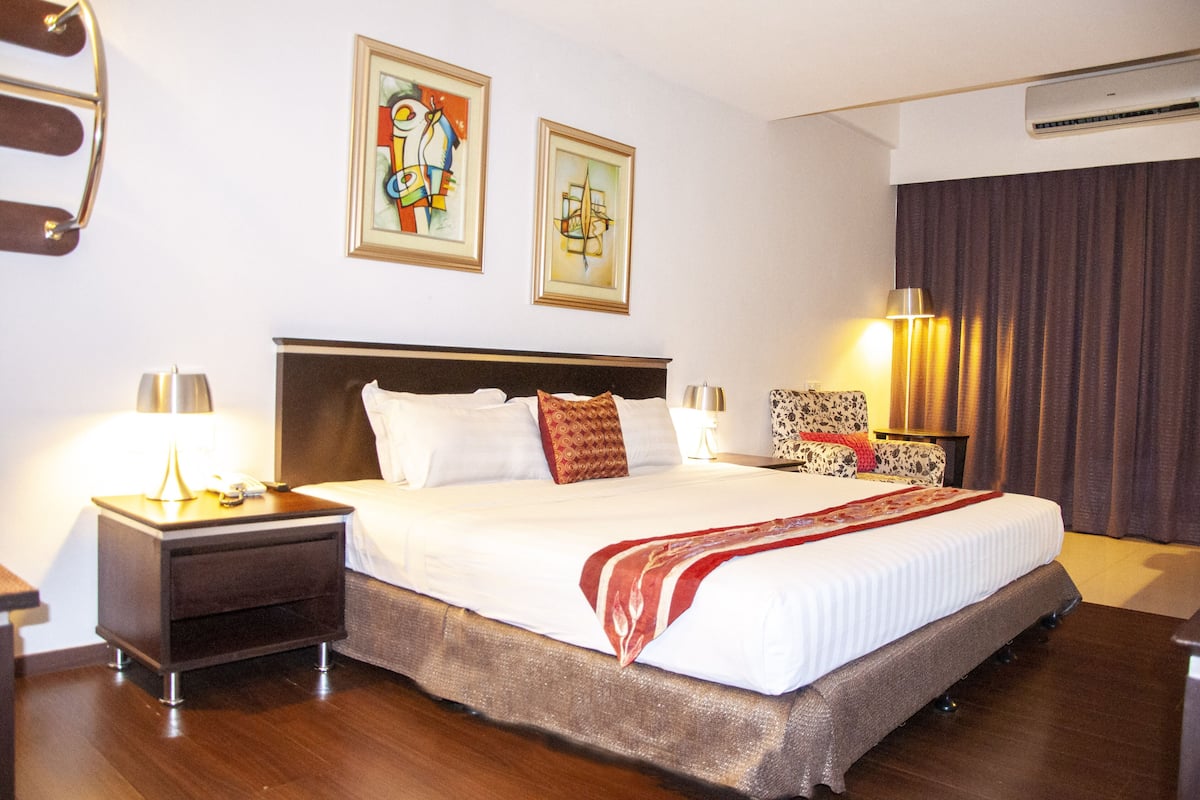 Habitación de hotel con una cama grande, dos mesitas de noche, una lámpara y dos cuadros en la pared.