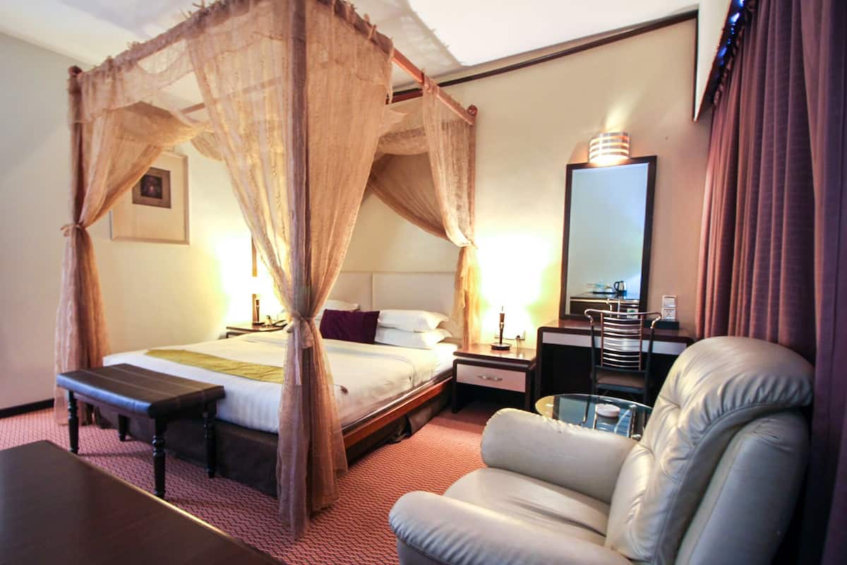 Una habitación de hotel con una cama con dosel, una mesita de noche, una silla, un escritorio y un espejo.