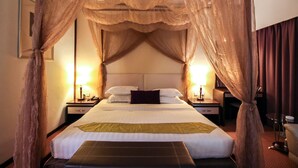 Une chambre d’hôtel avec un lit à baldaquin, des lampes de chevet, une table de chevet et une petite table avec une chaise.