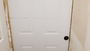 A white door with a black doormat, a wooden frame, and a light switch on the wall. - Save Time Commuting! North Side Suite 5 Min Walk to Site Bus Studio Basement (Fort McMurray)