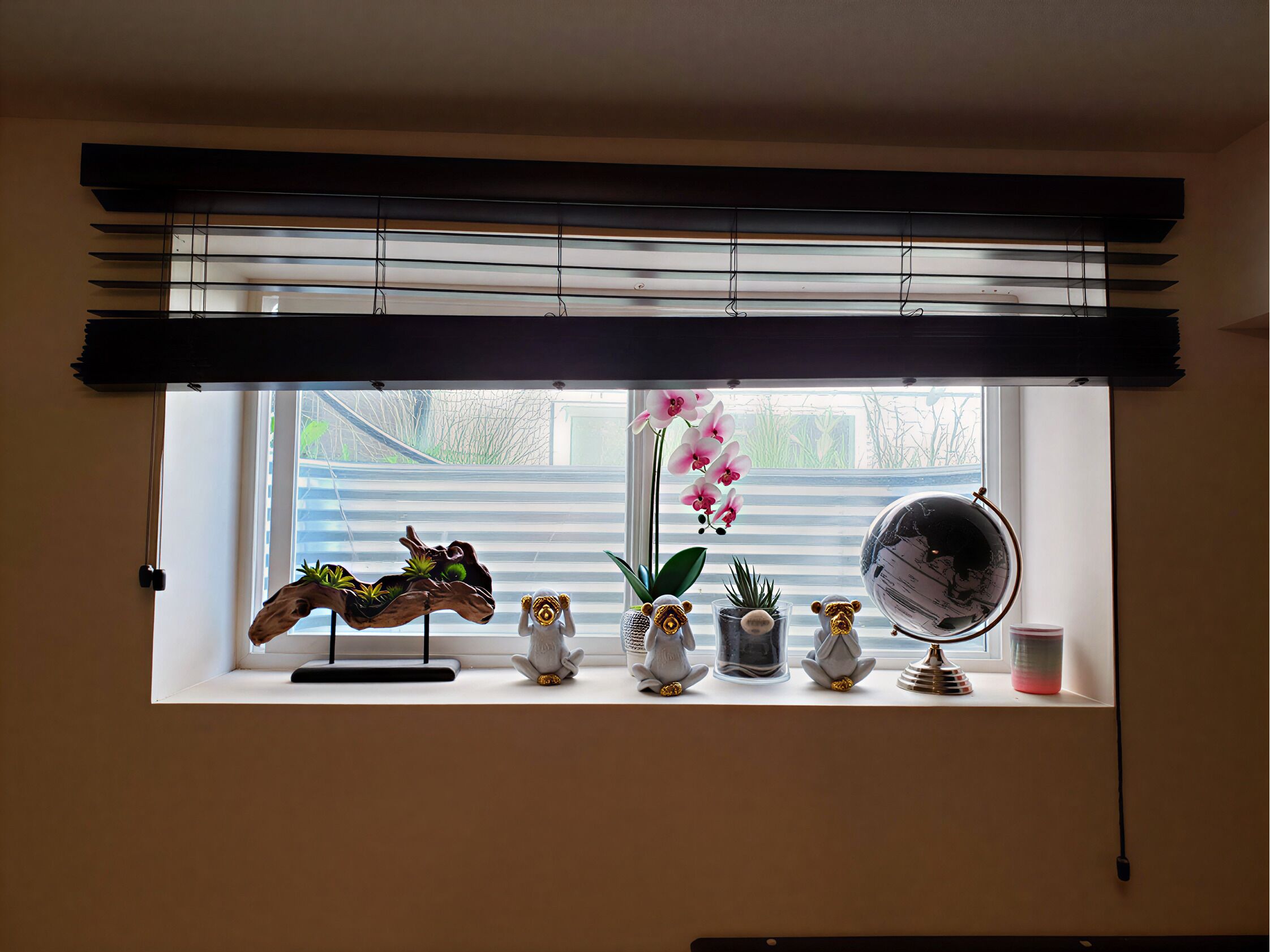 Una ventana con vistas a zonas verdes, un globo terráqueo y varios objetos decorativos en un estante.
