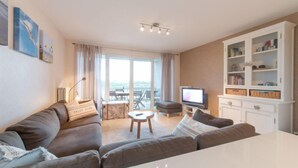 A modern living room with a large sofa, a small round table, a television, and a white cabinet with shelves. - D’Heyezicht with parking by Interhome (Bredene)