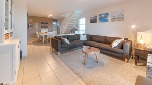 A spacious living area with a large sofa, a coffee table, and a dining area with a white table and chairs. A staircase leads to an upper level. - D’Heyezicht with parking by Interhome (Bredene)