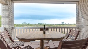 A covered patio with a round wooden table and four wooden chairs, a bottle of wine, and a glass on the table. - D’Heyezicht with parking by Interhome (Bredene)
