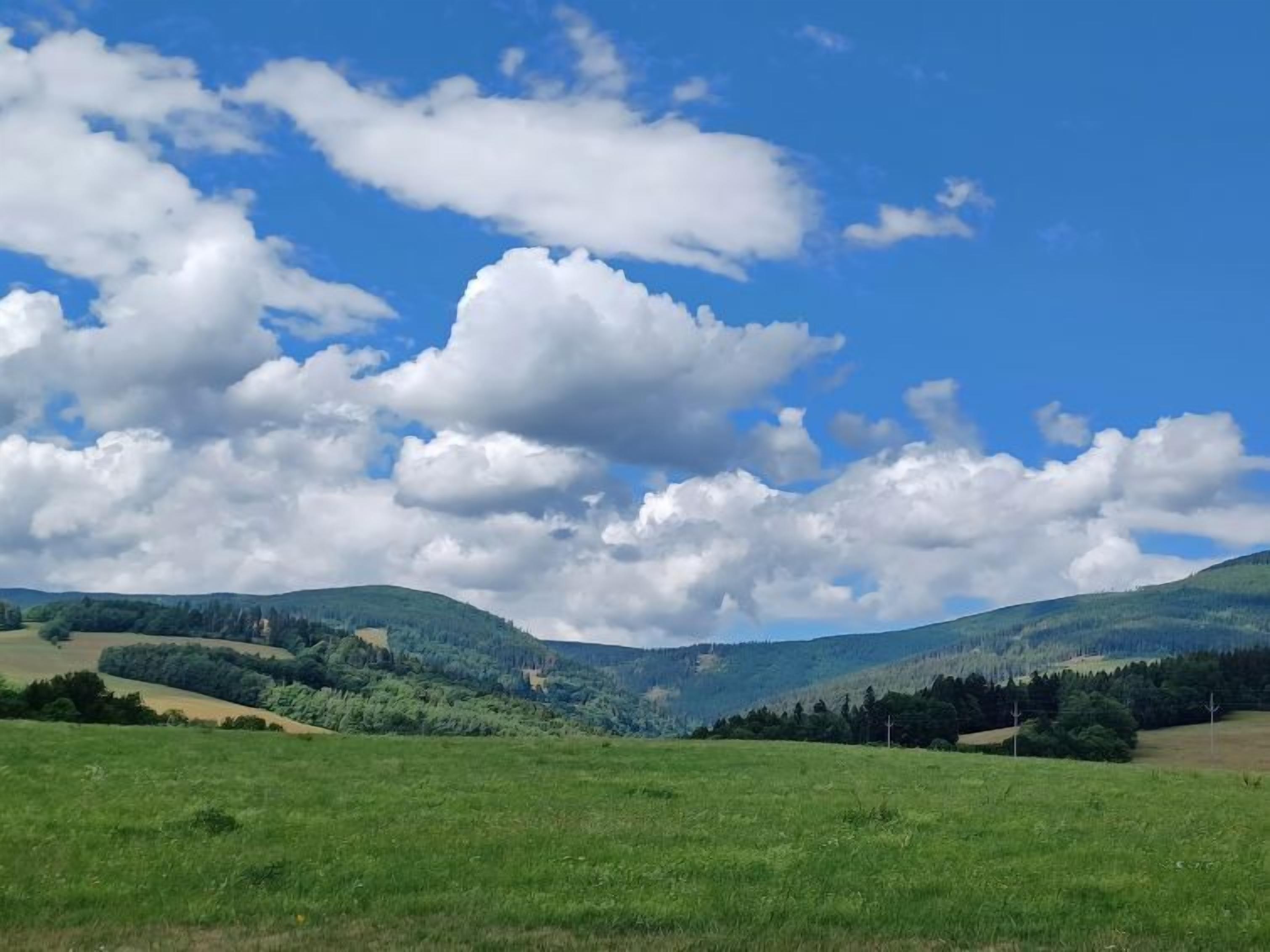 A panoramic view of a green field with rolling hills and a clear blue sky with scattered clouds.