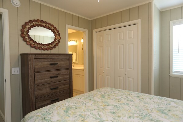 A bedroom with a wooden dresser, a bed with a floral bedspread, a mirror, and a white door.