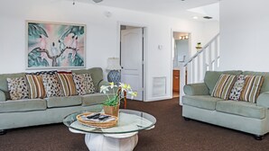 A living room with two green sofas, a glass coffee table, and a ceiling fan. - Beachfront, Quiet shoreline ~ Flamingo Dunes (St. Joe Beach)