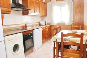A kitchen with wooden cabinets, a washing machine, an oven, and a dining table with chairs.