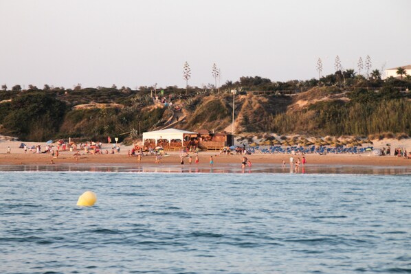 Una playa con gente, una torre de salvavidas y un edificio en la ladera.