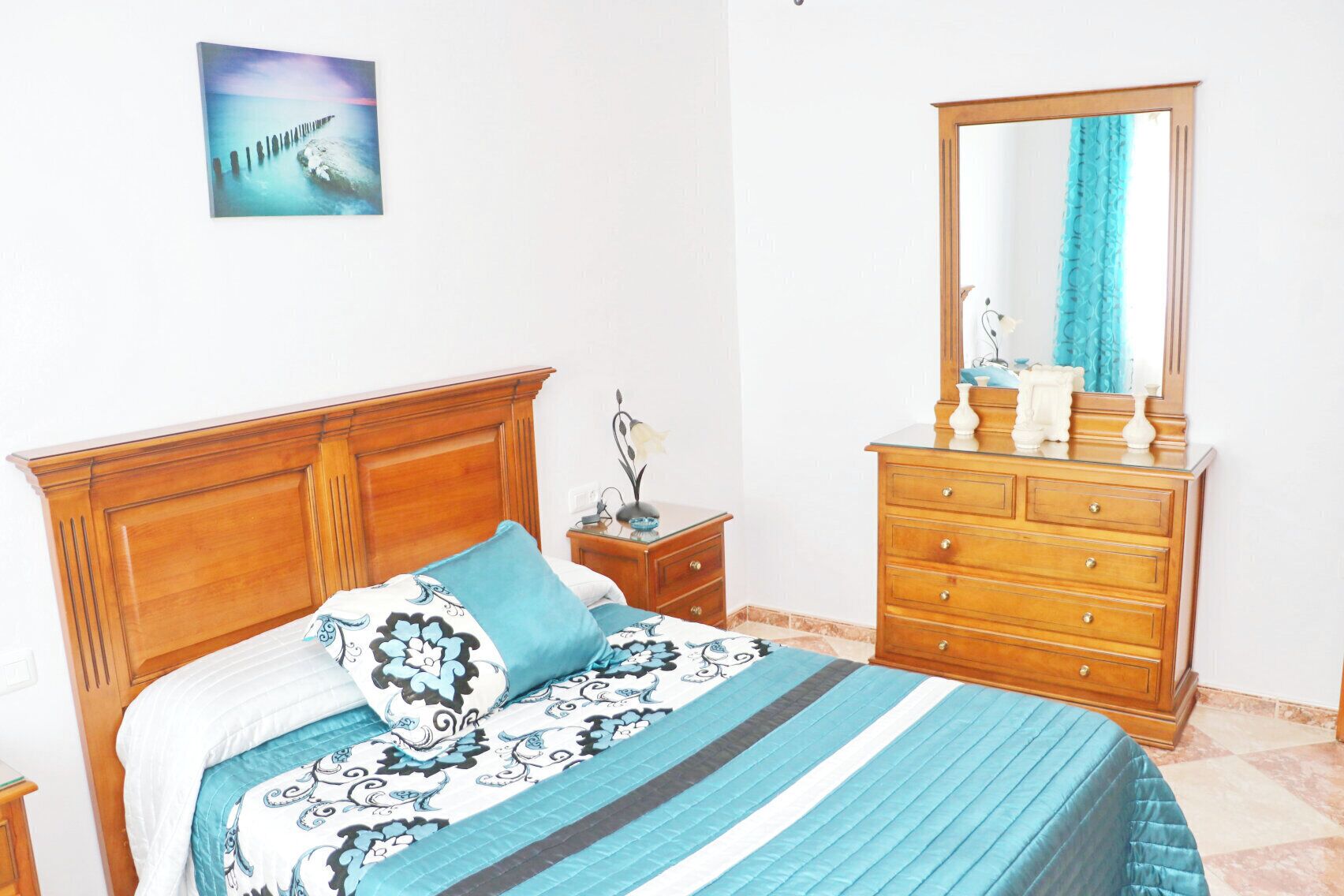 Une chambre à coucher avec un lit en bois, une commode, une table de chevet, un miroir et un tableau accroché au mur.