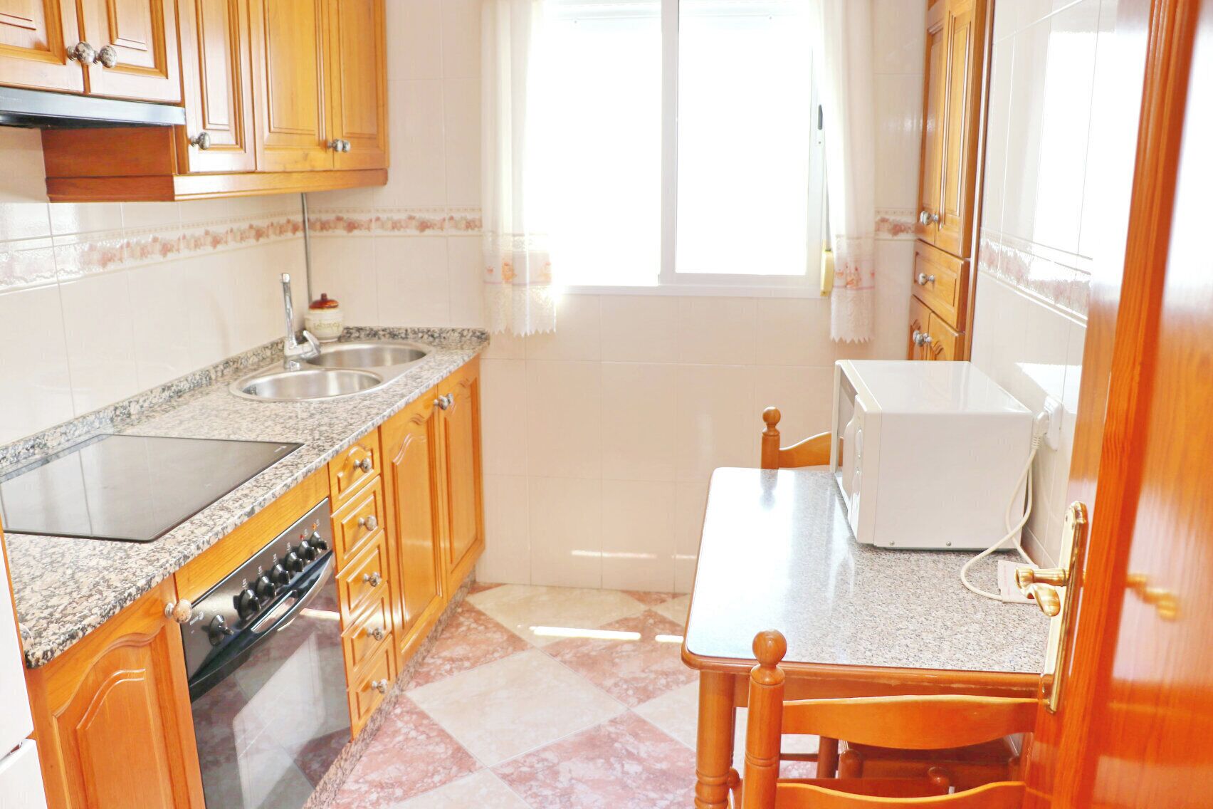 A compact kitchen with granite countertops, wooden cabinets, a built-in oven, a microwave, and a sink.