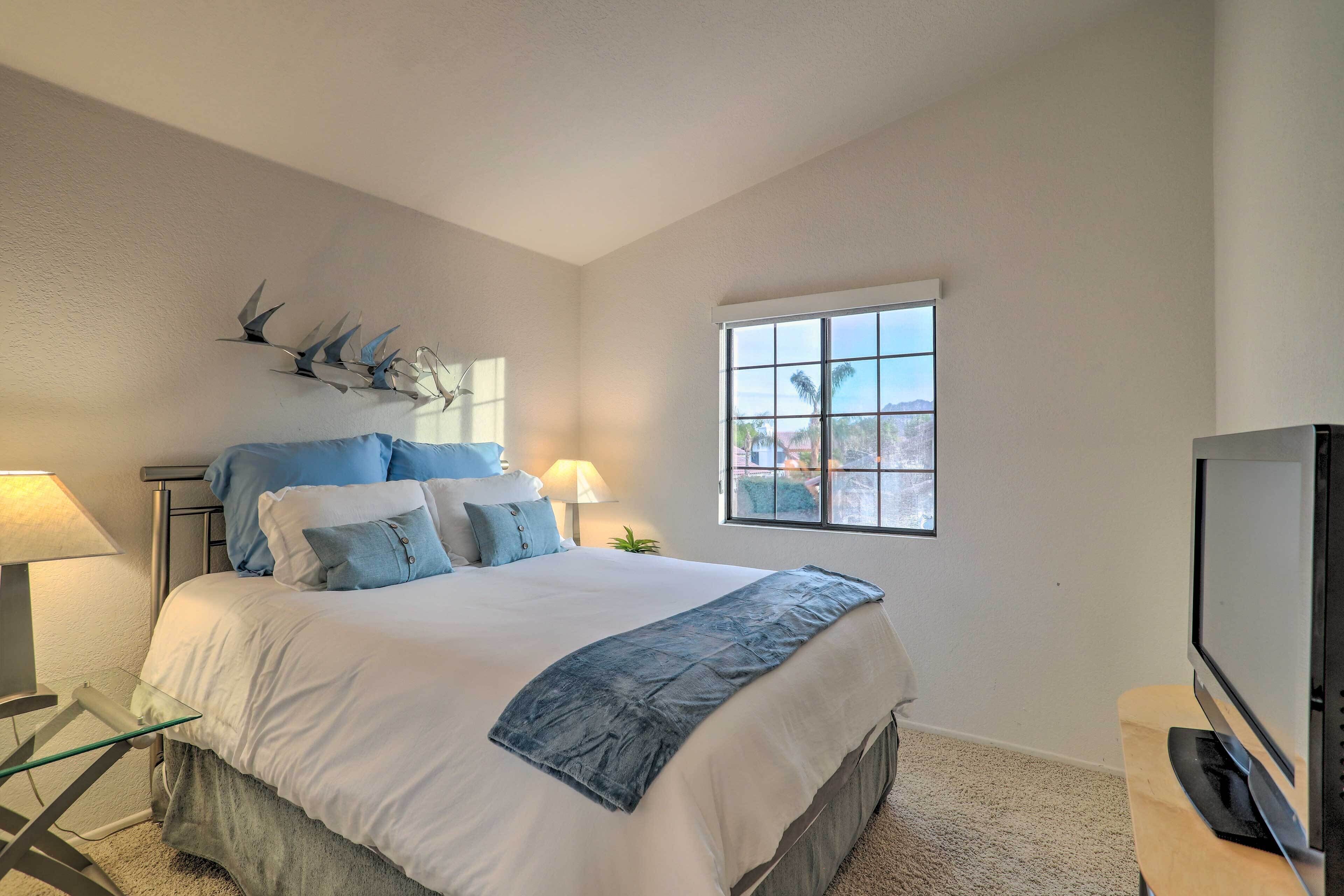 A bedroom with a bed, two bedside lamps, a window, and a television.