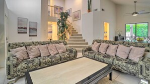 A spacious living room with patterned sofas, a central coffee table, a staircase, and a view of greenery outside. - Desert Oasis in La Quinta! Heated Pool & Patio (La Quinta)