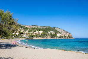 A beach with a clear blue sea, a sandy shore, and buildings on a hillside in the background. - Holiday Home "Sa Gola" with Private Pool, Terrace, Mountain Views & Wi-Fi (Canyamel)