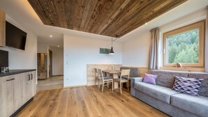 A modern interior with a wooden ceiling, a dining area with a table and chairs, a sofa with cushions, and a TV mounted on the wall. - Holiday Apartment "Lavendel" with Mountain View, Wi-Fi, Balcony & Sauna (Vöran)