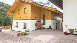 A two-story wooden house with a white exterior, a wooden porch, and a small garden area with potted plants. - Holiday Apartment "Lavendel" with Mountain View, Wi-Fi, Balcony & Sauna (Vöran)
