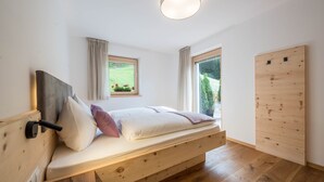 A bedroom with a wooden bed, two windows, a ceiling light, and a wooden wall panel. - Holiday Apartment "Lavendel" with Mountain View, Wi-Fi, Balcony & Sauna (Vöran)