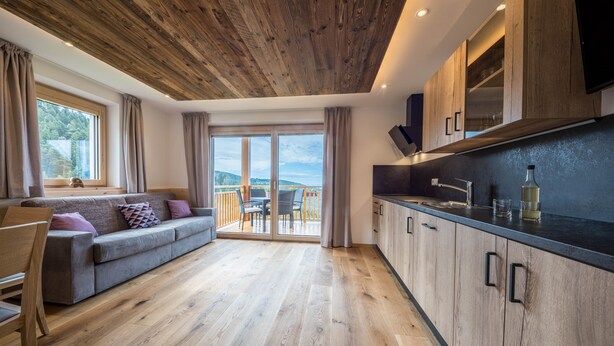 A modern kitchen with wooden cabinets and a dining area with a sofa and table. - Holiday Apartment "Lavendel" with Mountain View, Wi-Fi, Balcony & Sauna (Vöran)