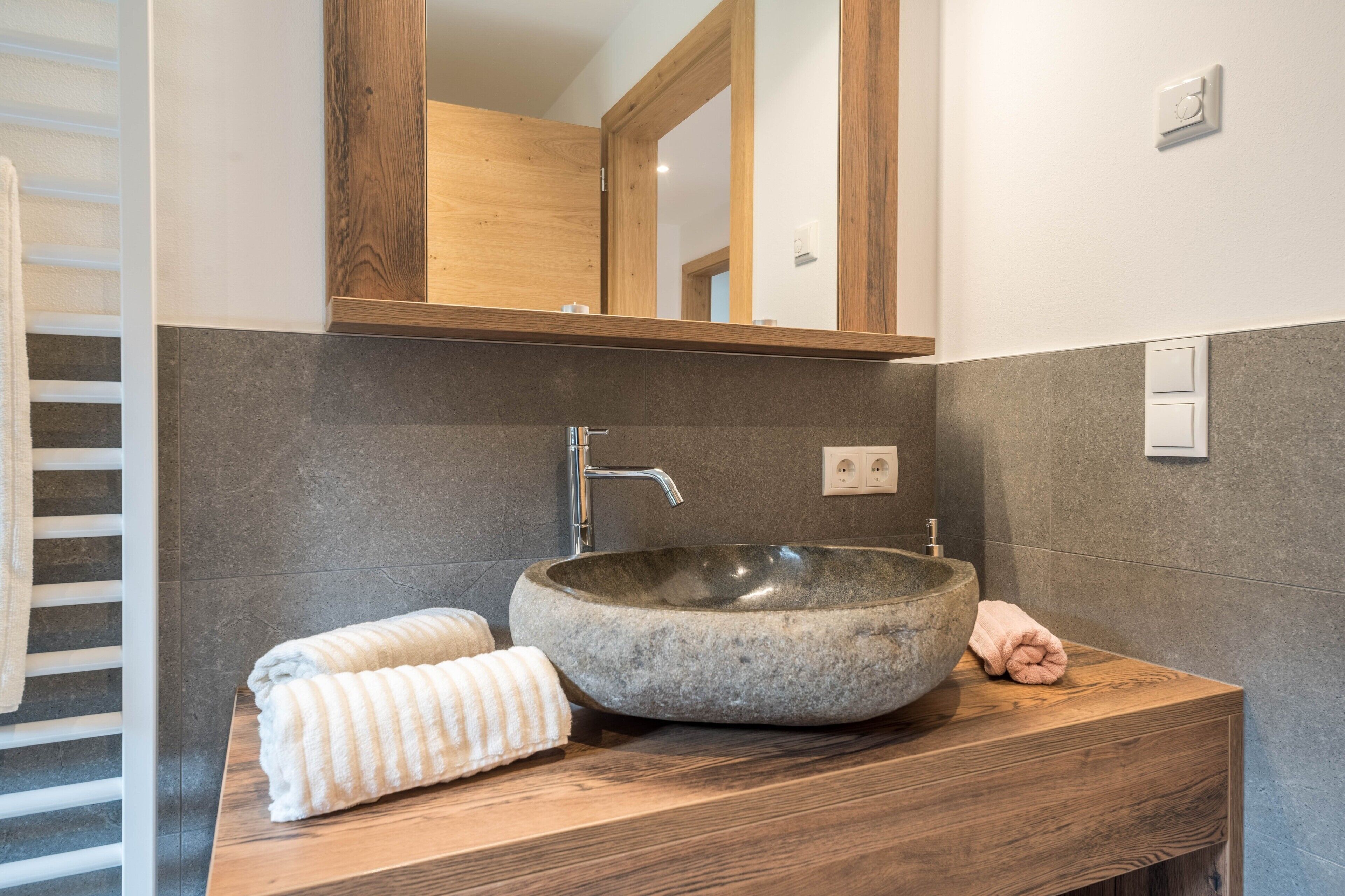 Ein Badezimmer mit einem SteinklopfZerbecken, einem Holzwaschtisch und einem Spiegel.