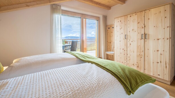 Un dormitorio con dos camas, un armario de madera y un balcón con mesa y sillas.