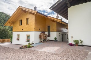A wooden house with a sloped roof, a brick entrance, and a gravel driveway.