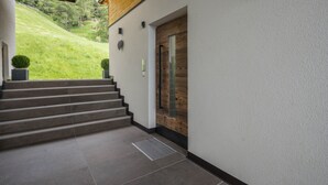 Ein moderner Gebäudeeingang mit einer Holztreppe, die zu einer Tür mit Glasfenster führt.