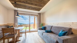 Ein modernes Zimmer mit Holzbalkendecke, einer Couch, einem Esstisch und Blick ins Freie.