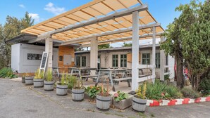 A covered outdoor seating area with wooden tables and chairs, surrounded by potted plants.