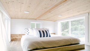 Ein Schlafzimmer mit einem großen Bett, Holzboden und großen Fenstern.