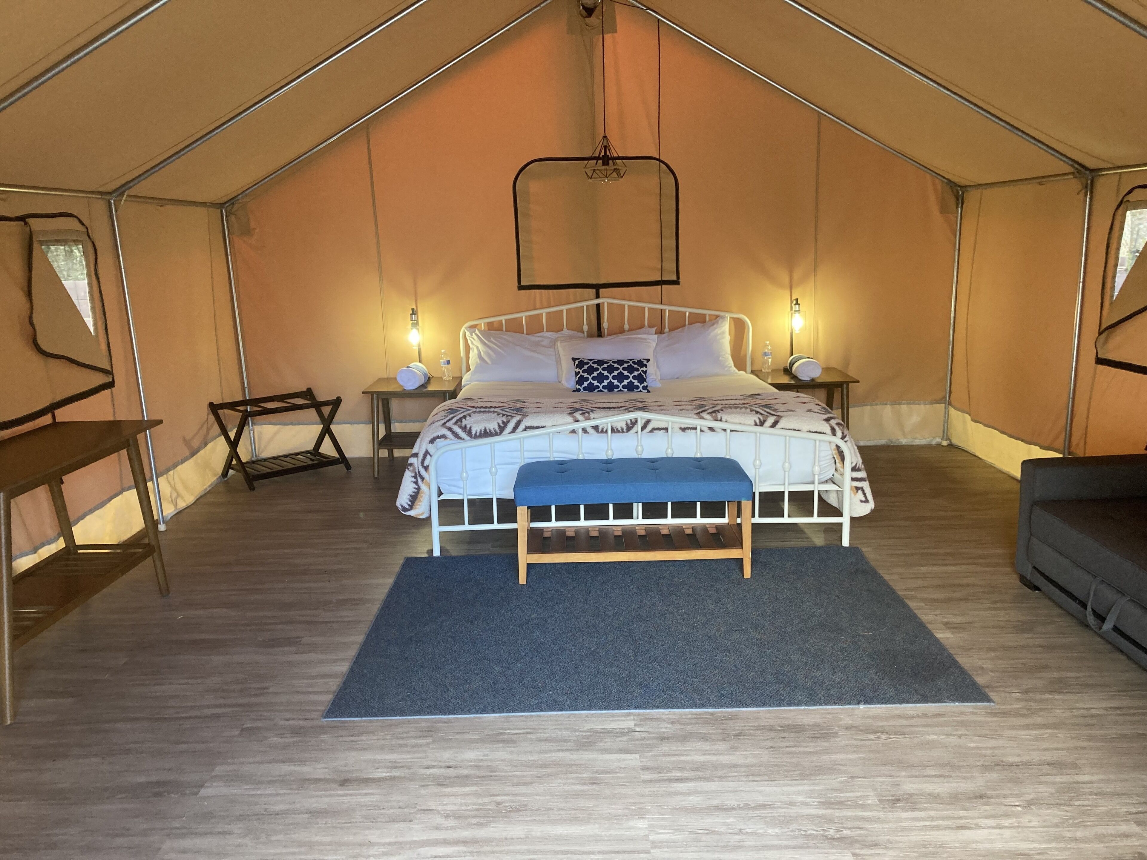 A tented room with a bed, bedside tables, a bench, and a hanging light fixture.