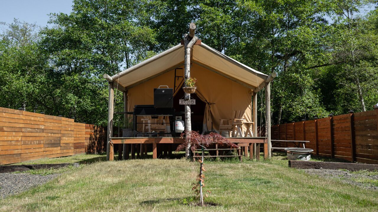 A tent with a wooden deck, a grill, and a hanging planter.