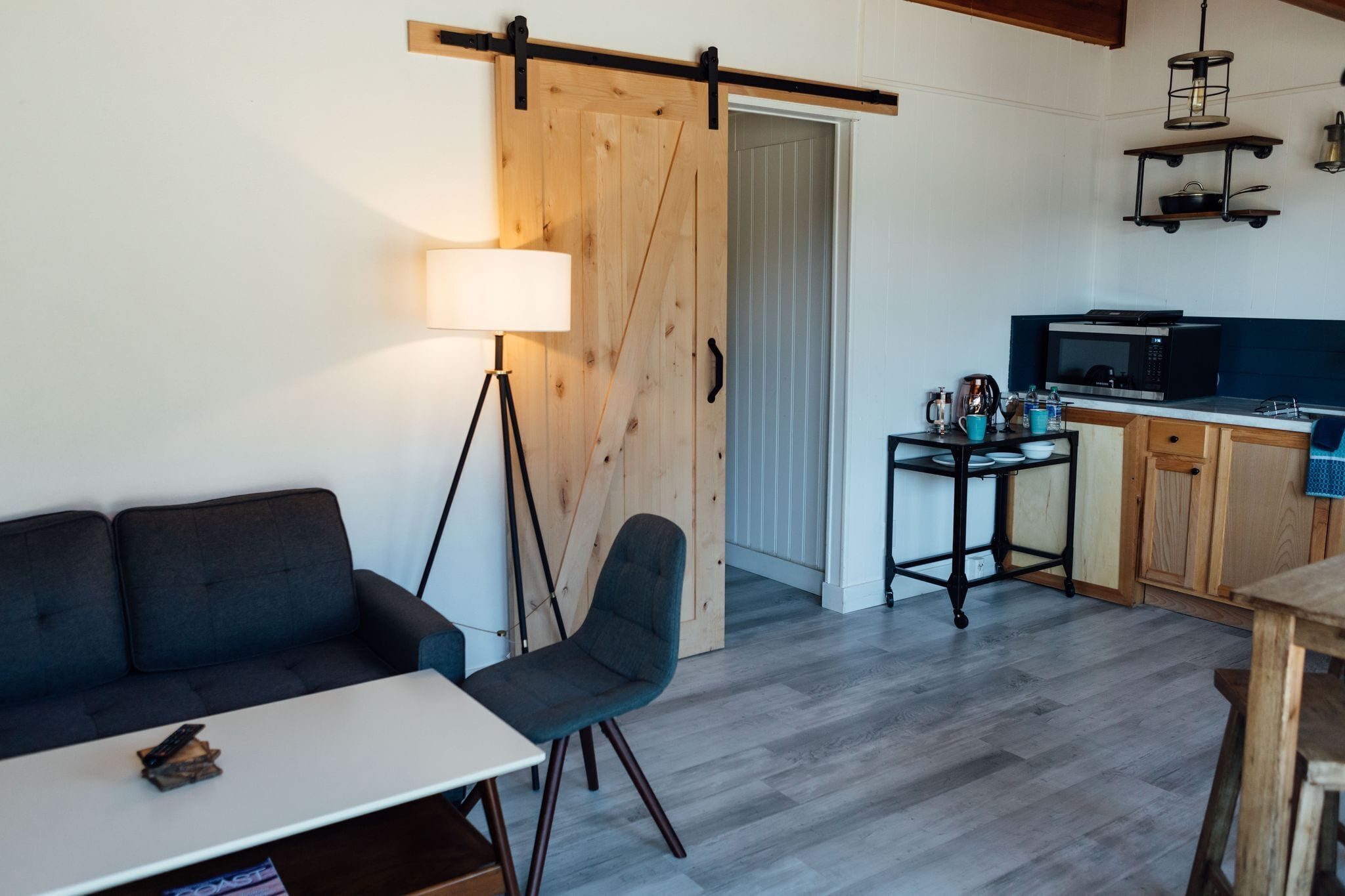 Um espaço de estar moderno com sofá, mesa de jantar, cadeira, luminária, área de cozinha com micro-ondas e uma porta de celeiro deslizante.