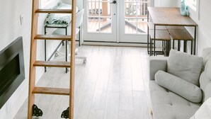 Ein Loft-Zimmer mit Holzbalkendecke, einem Schlafplatz im erhöhten Bereich, einer Couch, einem Tisch und einem an der Wand befestigten Fernseher.