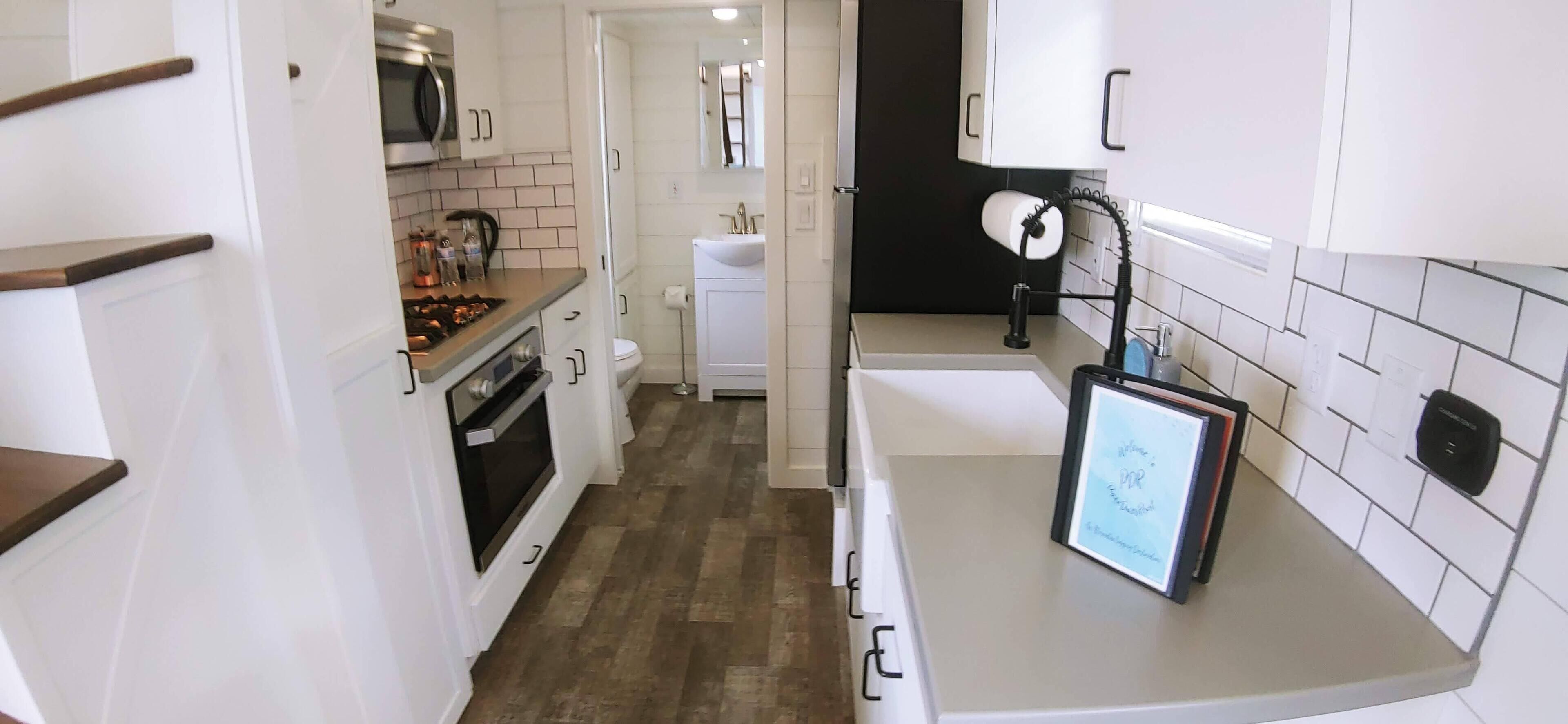 A compact kitchen with white cabinets, a microwave, a stove, and a sink.