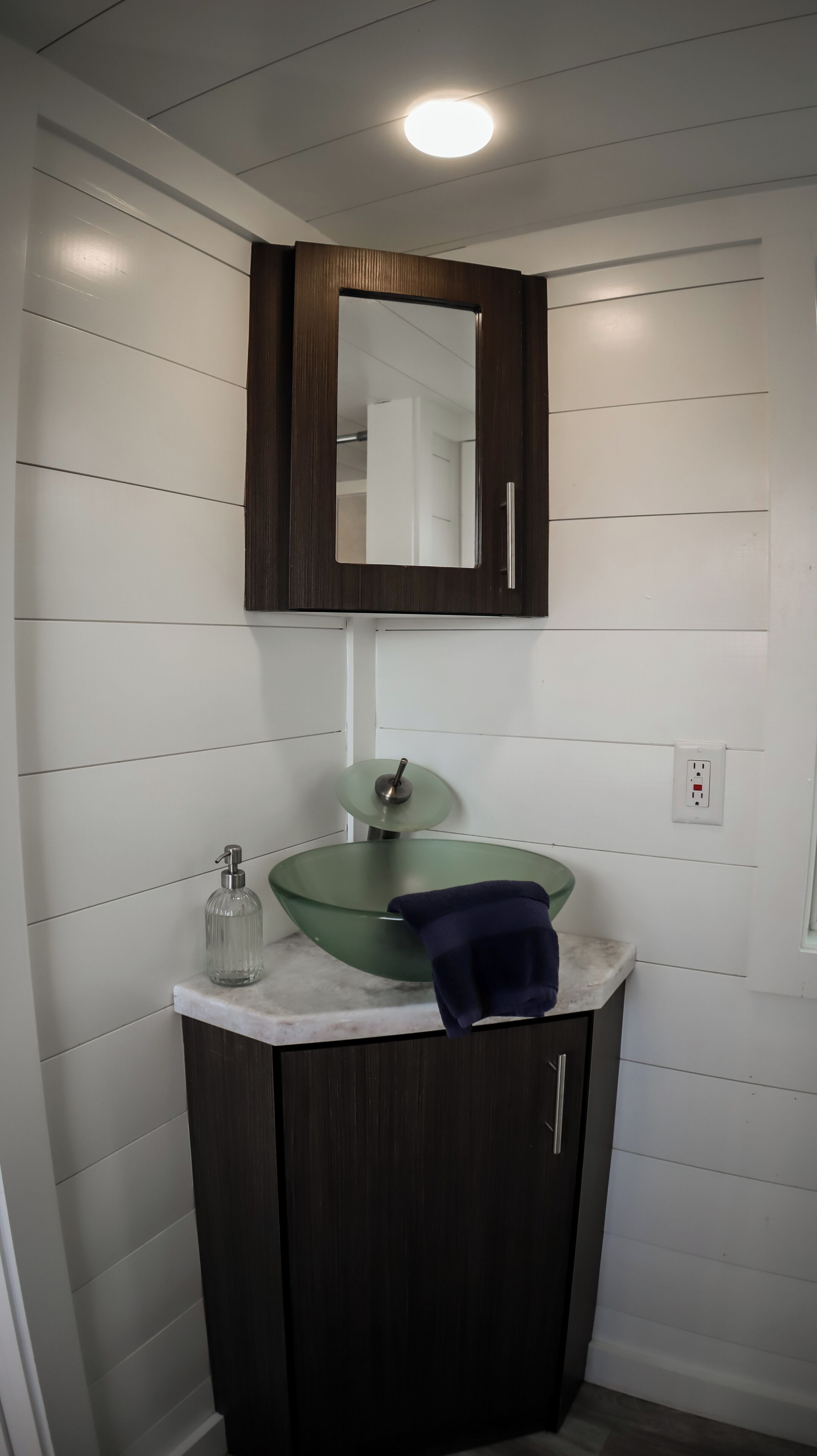 A bathroom with a glass sink, dark wooden cabinet, and a mirror above the sink.