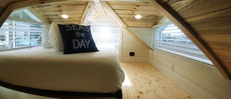 A bedroom with a bed, a pillow with "SEAS the DAY" text, wooden walls, and a window.